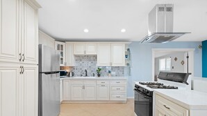 A modern kitchen with white cabinetry, a stainless steel refrigerator, a gas stove, and a microwave. - Moroccan Hacienda Retreat- By Festival Grounds (Indio)