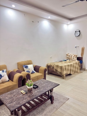 A living room with a sofa, a coffee table, a bed, and a clock on the wall.