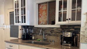 A kitchen with white cabinets, a stainless steel dishwasher, a coffee maker, and a window with a decorative curtain. - 3-bedroom Burbank Pool home close to studios and a Park across the street! (Burbank)