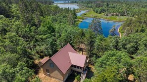 Una casa a un piano con tetto rosso, immersa in una fitta foresta, vicino a un lago.