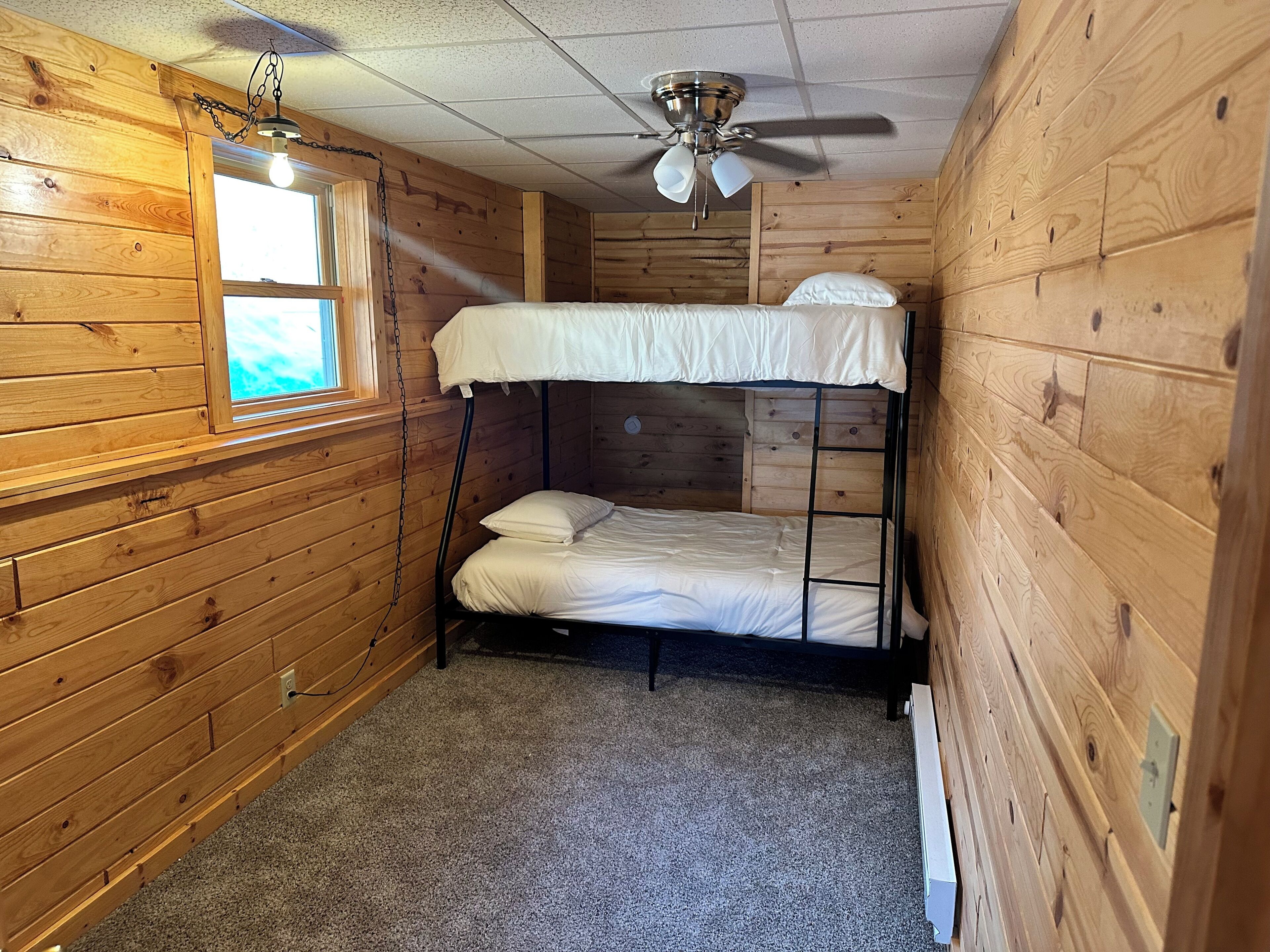 A bunk bed room with wooden walls, a ceiling fan, and a window.