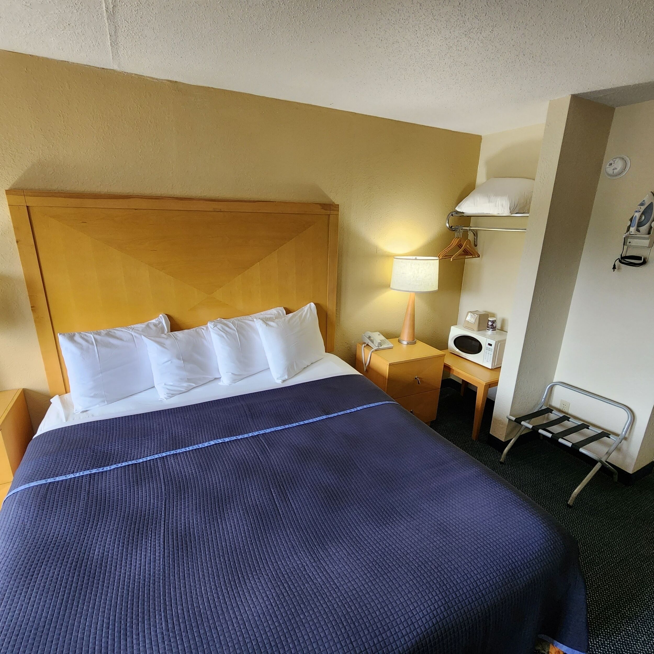 A hotel room with a bed, a bedside table with a lamp, a microwave, and a small ironing station.