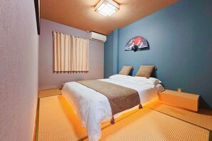 A room with a bed, a bedside table, a wall-mounted air conditioner, a window with curtains, and a decorative fan. - Friends Inn 友居 花園町201 两居室 日式和风民宿 (Osaka)