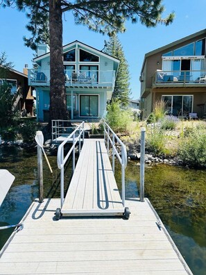 A wooden dock leading to a modern house with a balcony, situated by a body of water. - Emerald Oasis | Lakefront | Hot Tub | Boat Dock (South Lake Tahoe)