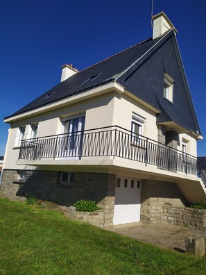 Ein zweistöckiges Haus mit Balkon, Stein Fundament und dunklem Dach.