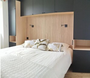 Ein Bett mit weißer Decke, zwei Kopfkissen mit Blättermuster und einem Holzbalkenkopf.