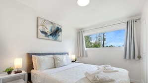 Un dormitorio con cama, mesitas de noche, una ventana con cortinas y un cuadro en la pared.
