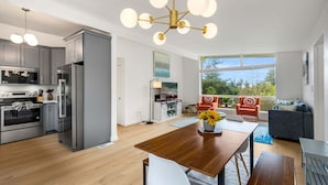 Una cocina moderna con electrodomésticos de acero inoxidable, una mesa de comedor de madera y un ventanal con vistas a un balcón.
