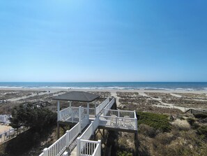 Blick auf einen Strand mit einer Holzpromenade, die zu einer Laube führt.