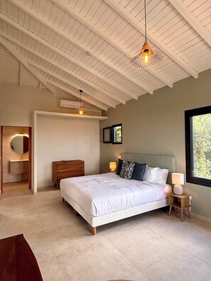 Une chambre à coucher avec un grand lit, une table de chevet en bois, un luminaire suspendu et une fenêtre donnant sur un beau paysage.
