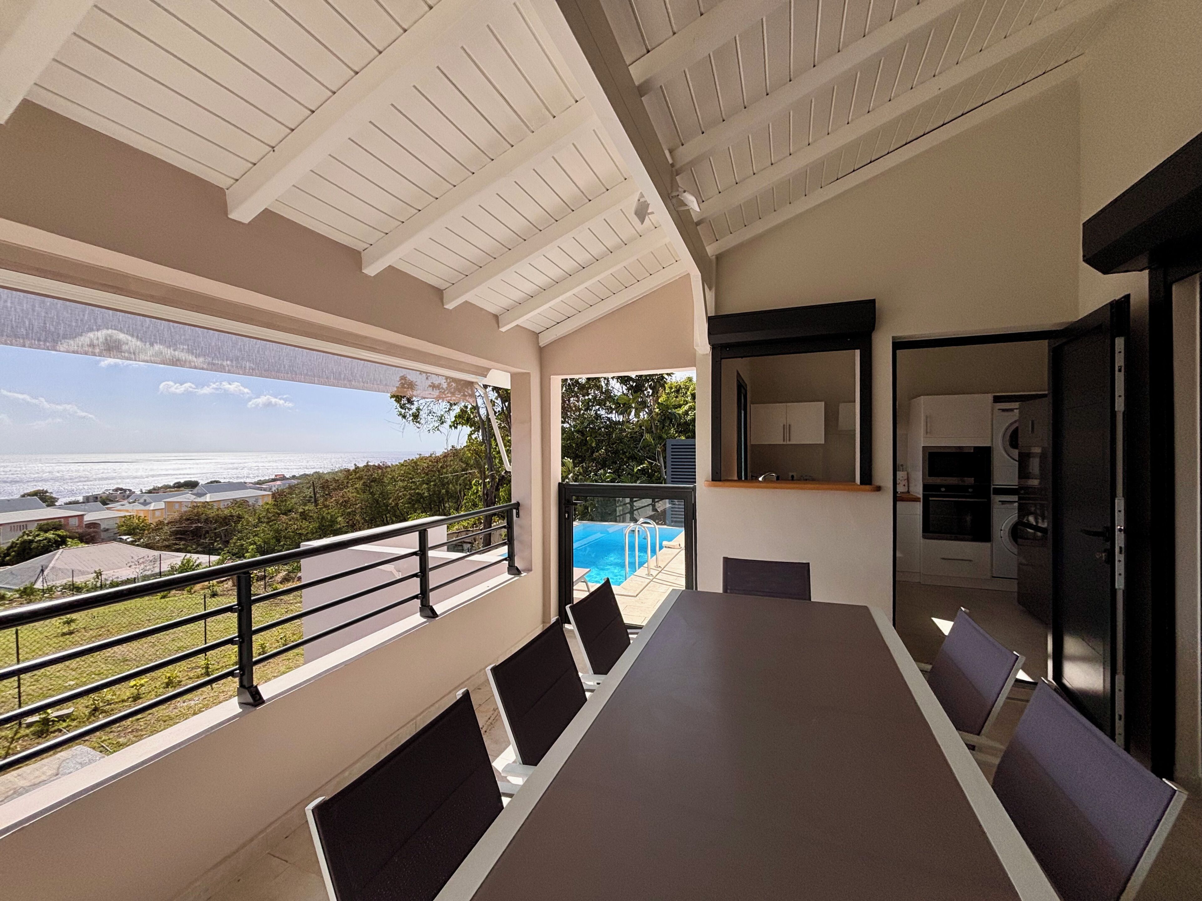 Un espacio de comedor al aire libre con techo, vista al mar, piscina y zona de cocina.