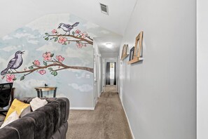 A hallway with a mural of birds on a branch, a couch, and framed pictures on the wall. - Cozy 2-bedroom family-friendly house featuring beautiful murals by local artist. (Brandon)