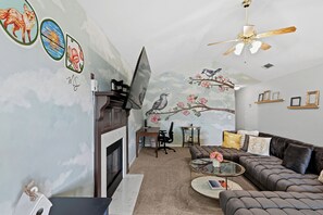 A living room with a fireplace, a sofa, a coffee table, and a TV. - Cozy 2-bedroom family-friendly house featuring beautiful murals by local artist. (Brandon)