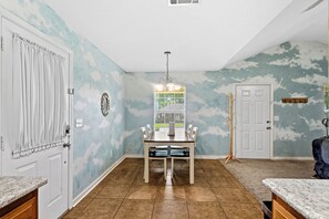 A dining area with a table and chairs, a chandelier, a coat rack, and a door with a coat stand. - Cozy 2-bedroom family-friendly house featuring beautiful murals by local artist. (Brandon)