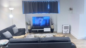 Una sala de estar moderna con un sofá grande y oscuro, un televisor de pantalla plana y piso de madera.