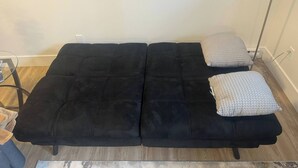 Un sofá negro con dos almohadas, una mesa de vidrio y piso de madera.