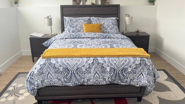 Un dormitorio con una colcha estampada, un plaid amarillo, dos mesitas de noche con lámparas y una alfombra floral.