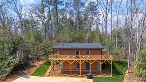 Une cabane en bois à deux étages, dotée d’une terrasse et entourée d’arbres.