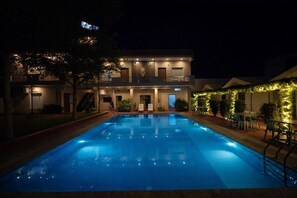 A swimming pool with a two-story building in the background, surrounded by greenery and outdoor seating. - KV Resort by Deevah Group (Pushkar)