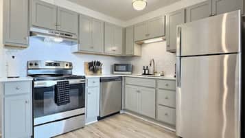 A modern kitchen with stainless steel appliances, grey cabinets, and a wooden floor.