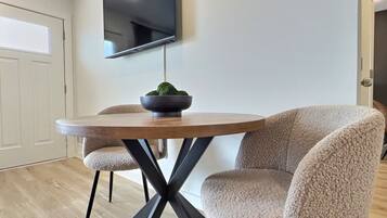 A dining area with a round table, two chairs, a bowl with a plant, and a mounted TV.