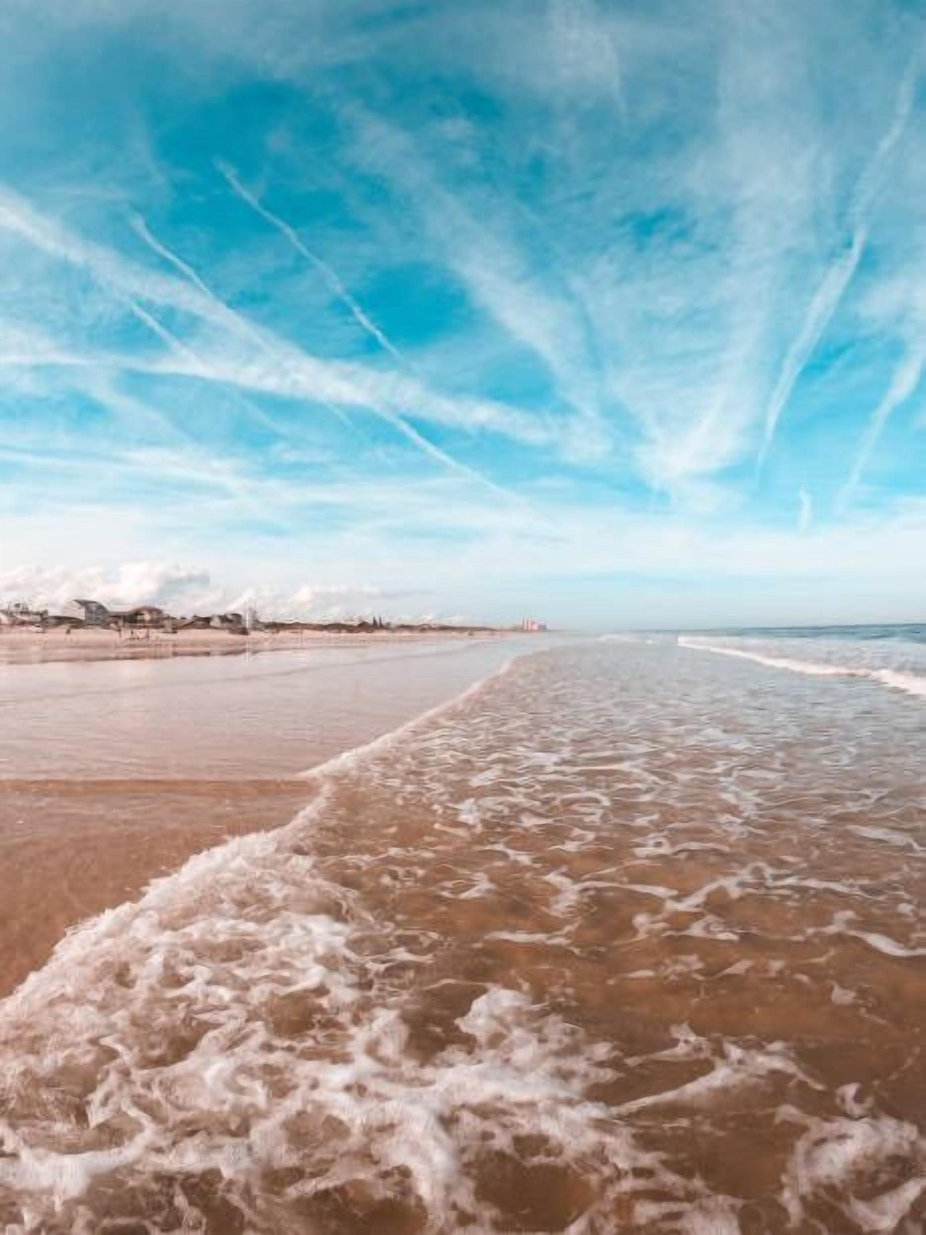 Una playa con olas, cielo despejado y edificios a lo lejos.