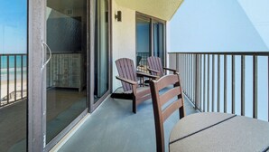 Un balcon avec une table et des chaises, une porte vitrée donnant sur une pièce et une vue sur la plage.