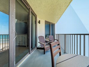 Ein Balkon mit Tisch und Stühlen, eine Glastür, die zu einem Zimmer führt, und Blick auf den Strand.