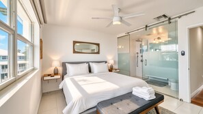 Une chambre d’hôtel comprenant un lit, des tables de chevet, un ventilateur de plafond, une douche en verre et une vue sur l’extérieur.