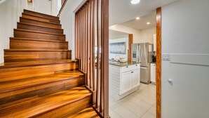 A wooden staircase leading to a kitchen area with white cabinetry and a stainless steel refrigerator. - 7 Mile Beach | Soft Sand, Epic Sunset Views & Shipwreck Snorkel (Grand Cayman)