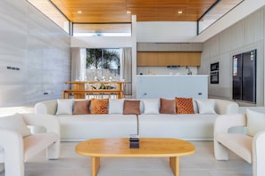 A modern living room with a sofa, coffee table, and kitchen in the background. - New Prime Location Near Boat Avenue V306 (Choeng Thale)