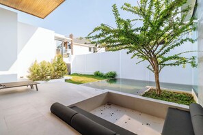 Un patio moderno al aire libre con una zona de estar, un árbol pequeño y vistas de un edificio.