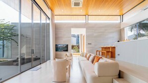 A modern living room with a large sectional sofa, a glass wall, and a wooden ceiling. - New Prime Location Near Boat Avenue V306 (Choeng Thale)