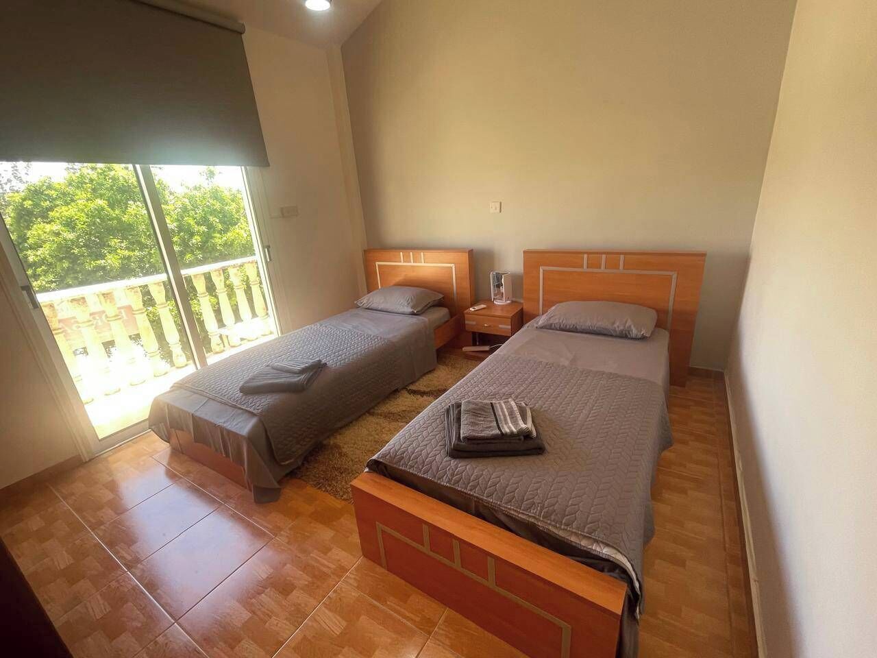 Une chambre avec deux lits simples, une tête de lit en bois, une table de chevet et une grande fenêtre donnant sur un paysage verdoyant.
