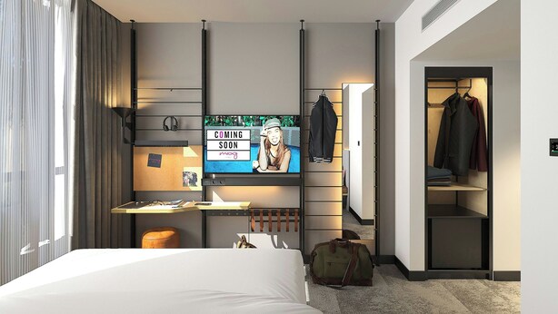 Ein Hotelzimmer mit Bett, Schreibtisch mit Computer, Fernseher, Kleiderständer und Schrank.