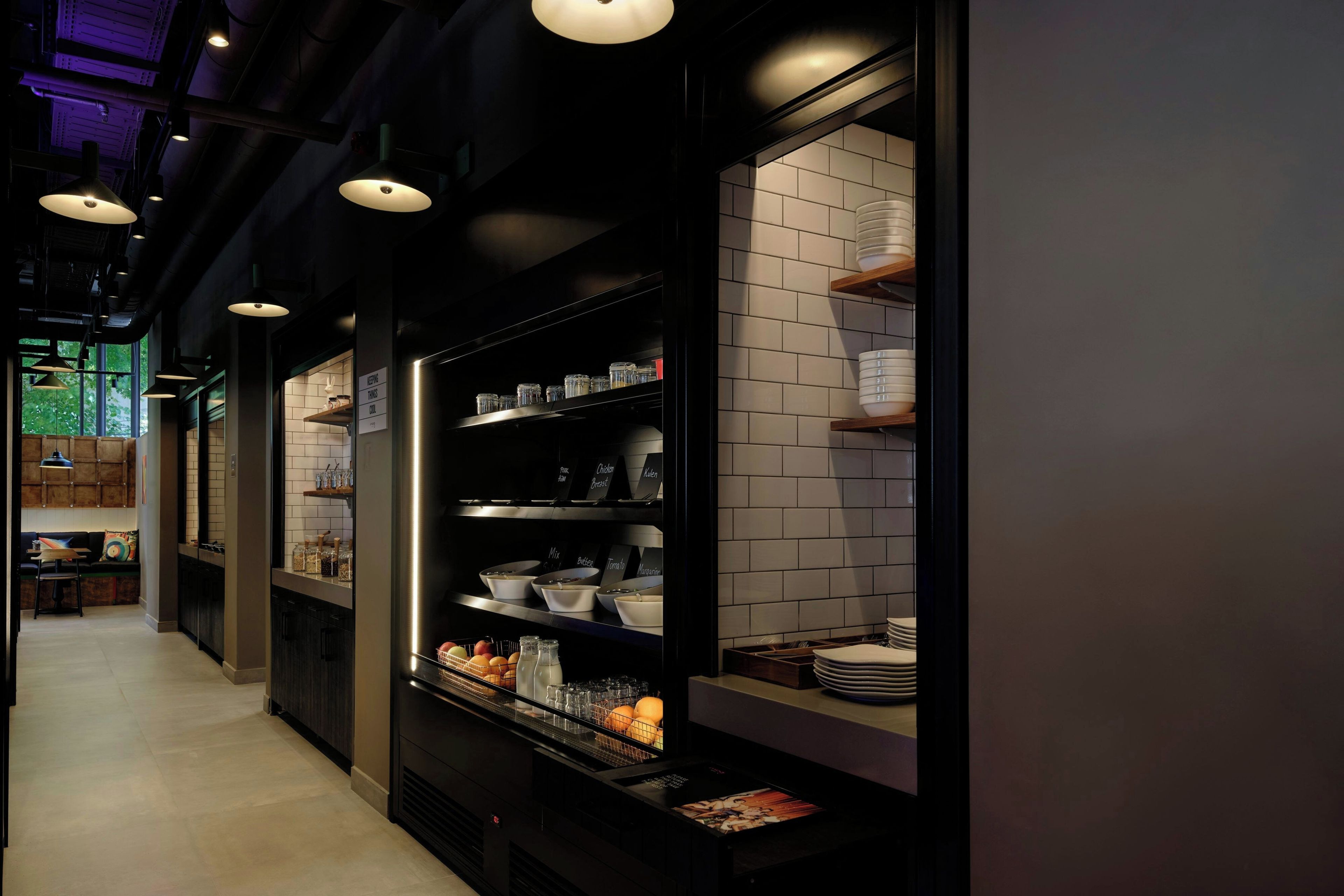 A modern kitchen with black cabinetry, white tiled backsplash, and overhead pendant lighting.