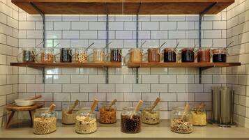 Una cocina con dos repisas de madera que sostienen frascos con alimentos y una encimera con frascos de cereales y nueces.
