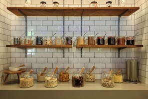 A kitchen with two wooden shelves holding jars of food items and a countertop with jars of cereal and nuts.