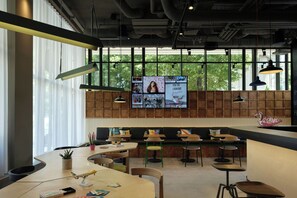 A modern cafe with a large window, wooden panel wall, and multiple seating areas. - Moxy Belgrade Skadarlija (Belgrade)