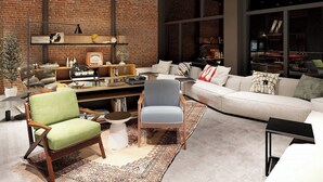 Ein modernes Wohnzimmer mit Backsteinwand, einem weißen Sofa, einem grünen Sessel und einem blau gemusterten Stuhl.