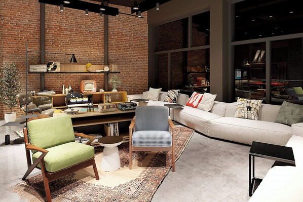 Un salon moderne avec un mur en briques, un canapé blanc, un fauteuil vert et une chaise à motifs bleus.
