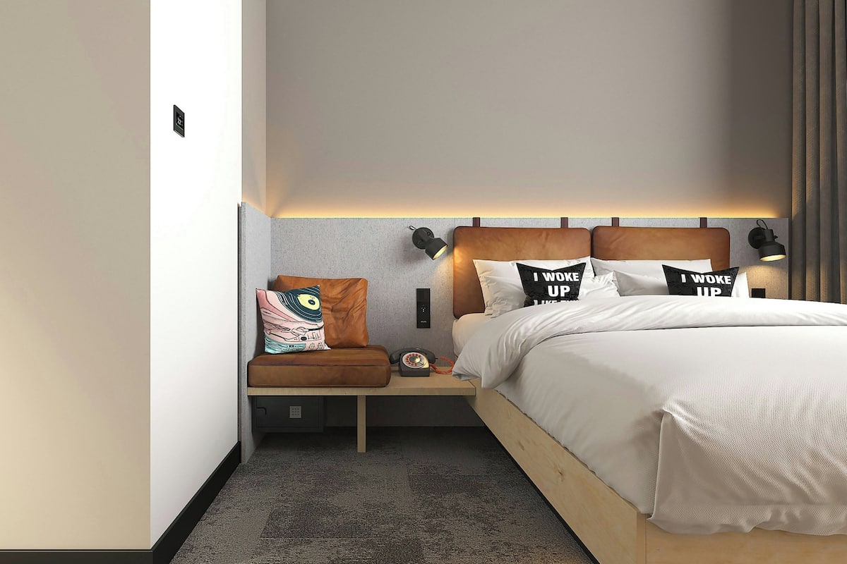 Una habitación de hotel moderna con una cama, mesitas de noche y una lámpara de pared.