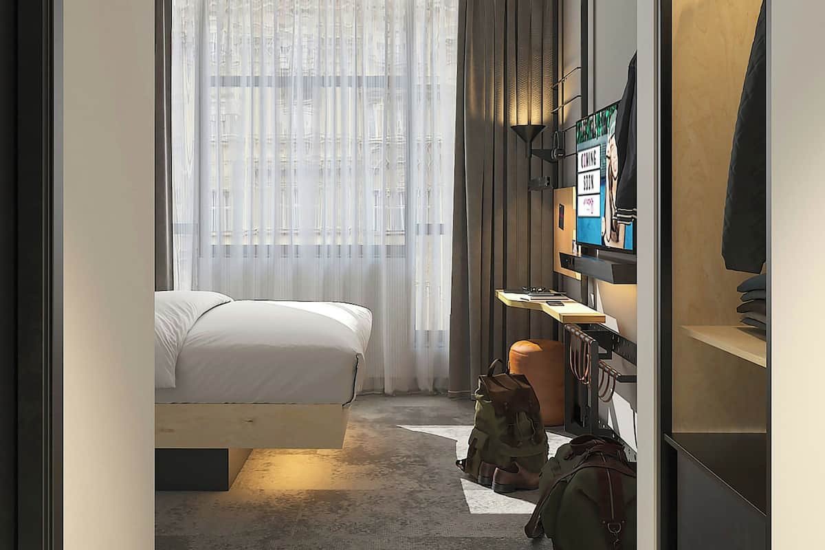 Una habitación de hotel con una cama, televisión, escritorio y armario.