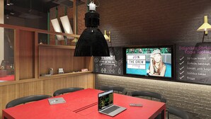 Ein modernes Interieur mit einem roten Tisch, einem Laptop, einem Fernseher, der eine Willkommensbotschaft anzeigt, und einer Kreidetafel mit Speisenangebot.