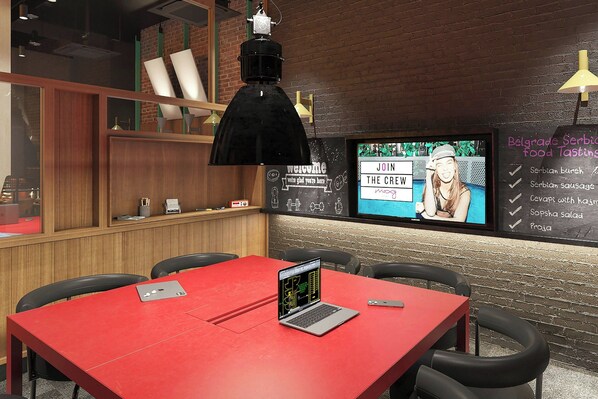 Un intérieur moderne avec une table rouge, un ordinateur portable, un téléviseur affichant un message de bienvenue et un tableau noir servant de menu, sur lequel sont indiquées les différentes options de plats.