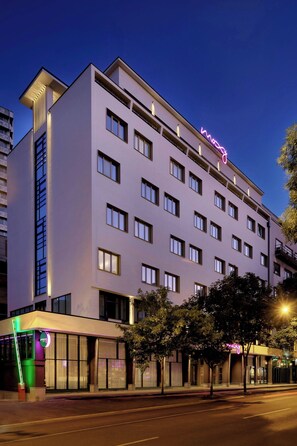 Un hôtel à plusieurs étages, doté d’une façade moderne, de grandes fenêtres et d’une enseigne lumineuse bien visible.