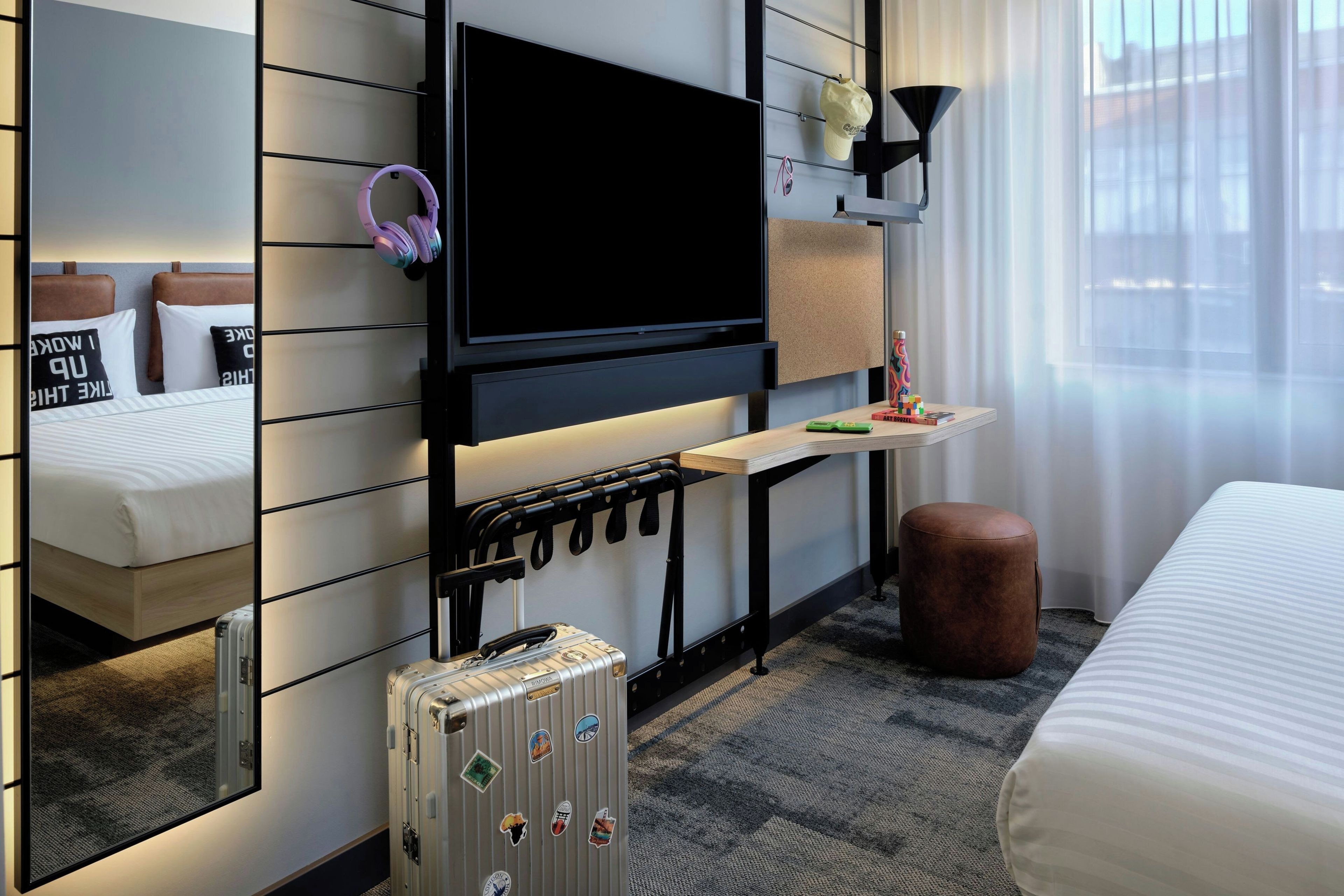 Une chambre d’hôtel moderne équipée d’un lit, d’un téléviseur à écran plat, d’un bureau avec une lampe, d’une valise et d’un porte-manteau mural.
