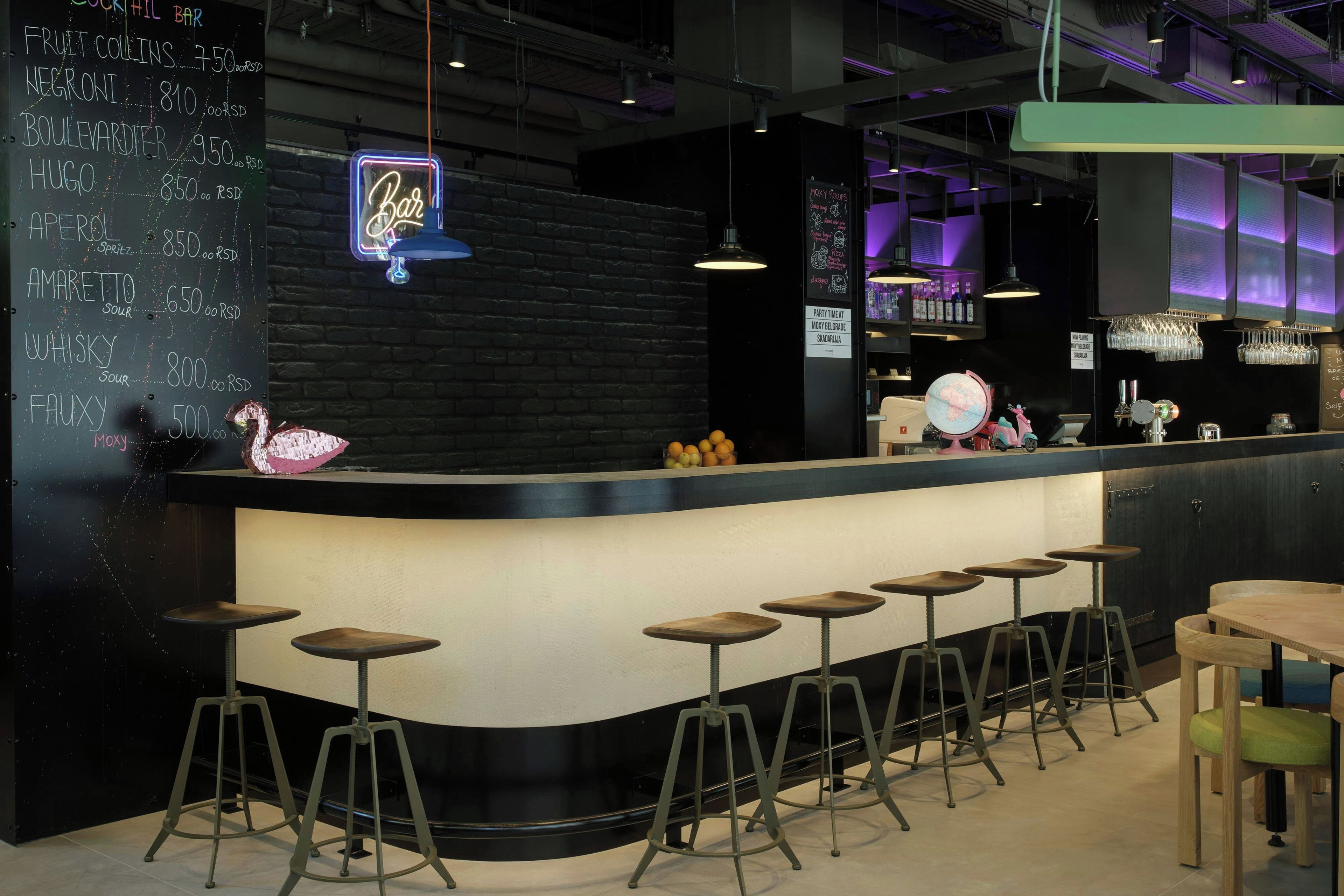A bar area with a neon sign, a chalkboard menu, and bar stools.