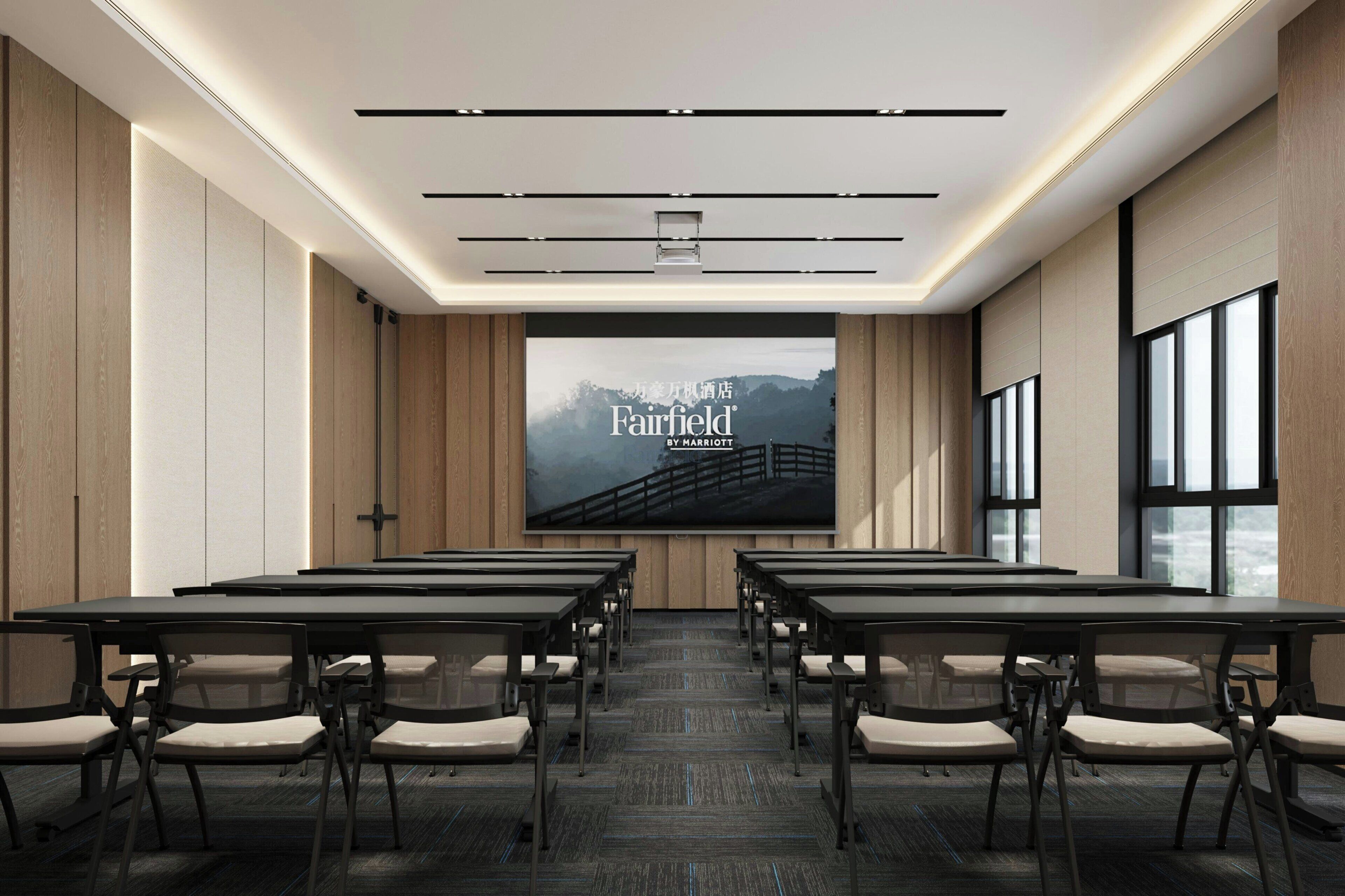 A conference room with a large screen displaying 'Fairfield by Marriott,' rows of tables and chairs, and large windows on one side.