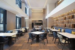 Un espace de restauration moderne, doté de plusieurs tables et chaises, d’une colonne centrale et d’un mur agrémenté de panneaux lumineux.